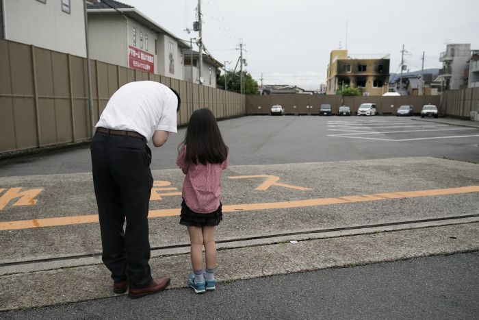 一名男子和他的女兒於縱火案後，在京都動畫工作室大樓外遠處，為大火受害者祈禱。(來源：美聯社)